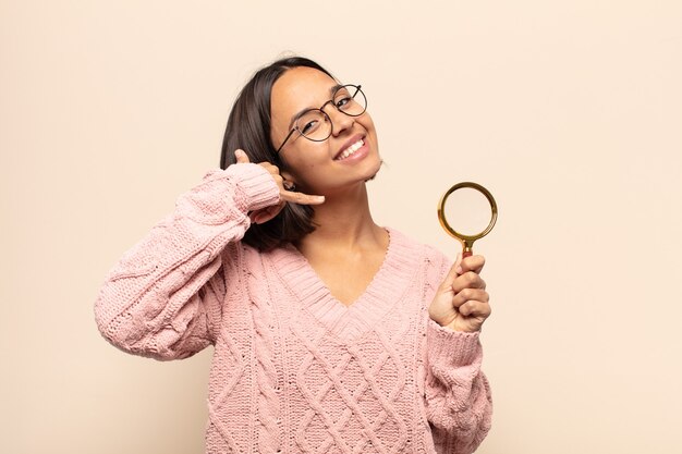 Young hispanic woman smiling cheerfully and pointing to camera while making a call you later gesture, talking on phone