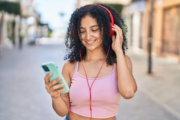 Young hispanic woman smiling confident listening to music at street