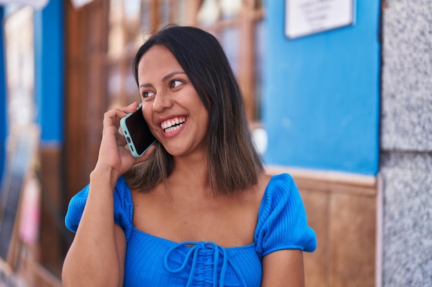 Young hispanic woman smiling confident talking on the smartphone at street