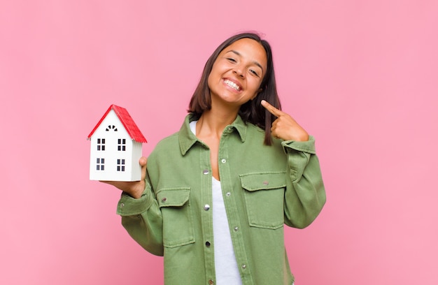 Young hispanic woman smiling confidently pointing to own broad smile, positive, relaxed, satisfied attitude