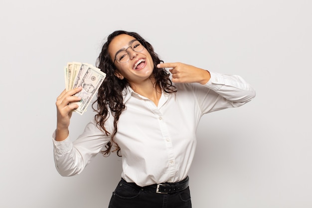 Young hispanic woman smiling confidently pointing to own broad smile, positive, relaxed, satisfied attitude