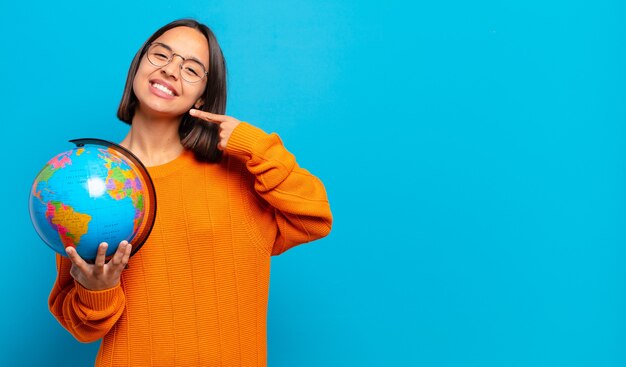 Young hispanic woman smiling confidently pointing to own broad smile, positive, relaxed, satisfied attitude