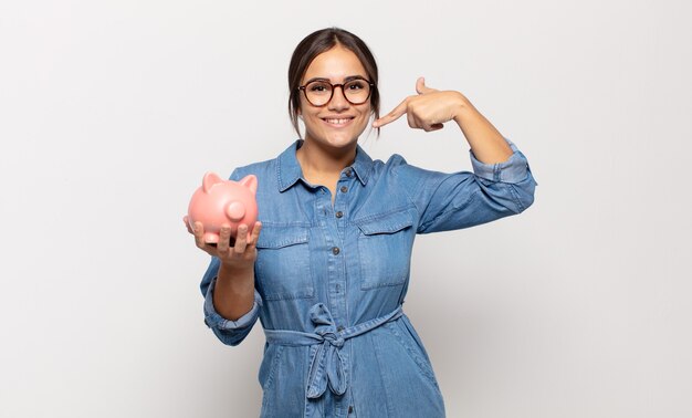 Young hispanic woman smiling confidently pointing to own broad smile, positive, relaxed, satisfied attitude