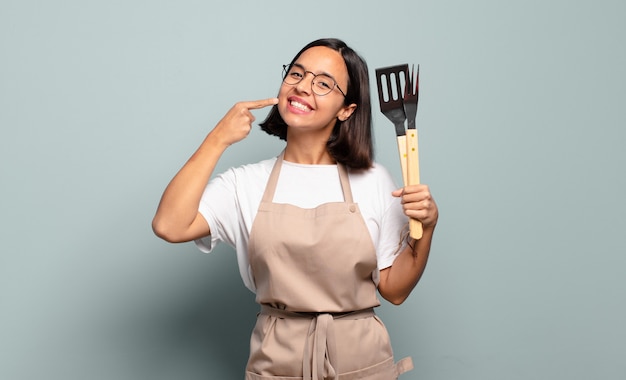 Young hispanic woman smiling confidently pointing to own broad smile, positive, relaxed, satisfied attitude