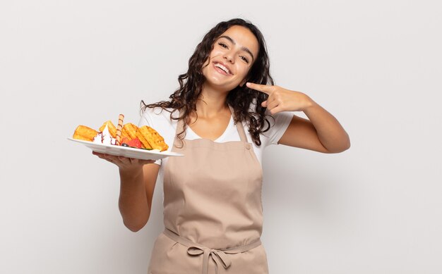 Young hispanic woman smiling confidently pointing to own broad smile, positive, relaxed, satisfied attitude