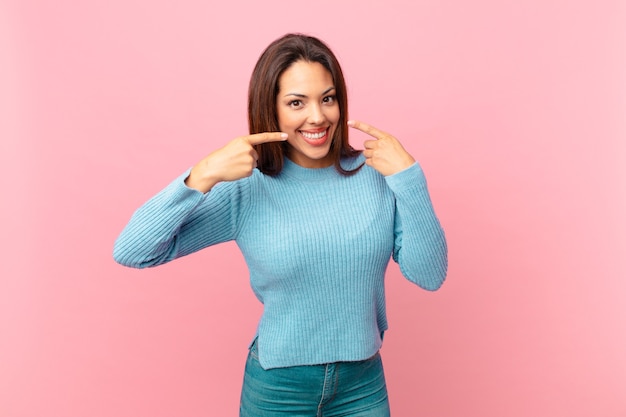 young hispanic woman smiling confidently pointing to own broad smile