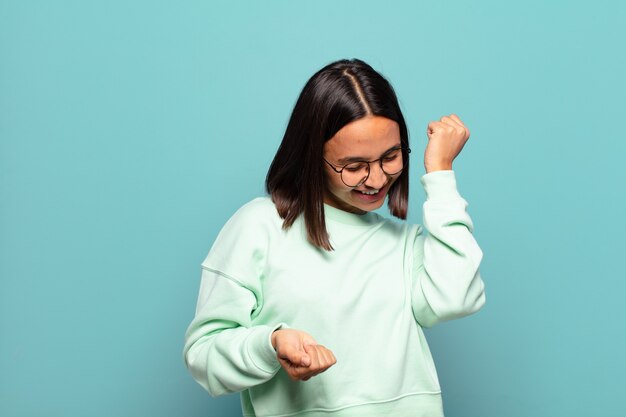 Young hispanic woman smiling, feeling carefree, relaxed and happy, dancing and listening to music, having fun at a party