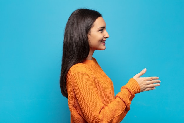 Young hispanic woman smiling, greeting you and offering a hand shake to close a successful deal, cooperation concept