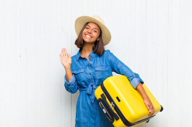 Young hispanic woman smiling happily and cheerfully, waving hand, welcoming and greeting you, or saying goodbye