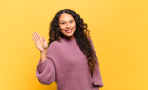 Photo young hispanic woman smiling happily and cheerfully, waving hand, welcoming and greeting you, or saying goodbye