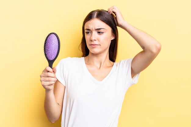 幸せに笑って、空想にふけったり、疑ったりする若いヒスパニック系女性。ヘアブラシのコンセプト