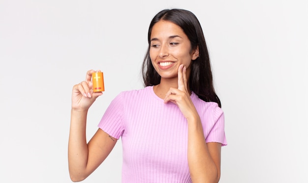 Young hispanic woman smiling happily and daydreaming or doubting and holding batteries