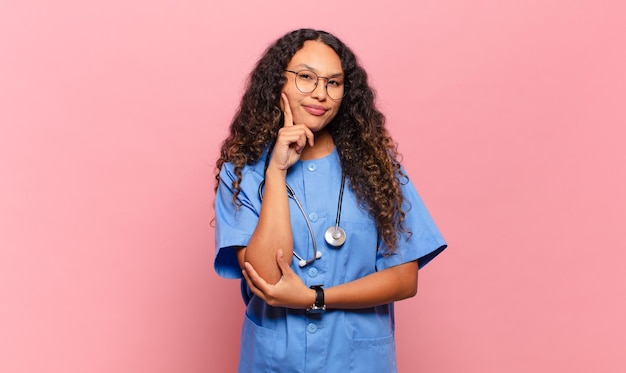Photo young hispanic woman smiling happily and daydreaming or doubting, looking to the side. nurse concept