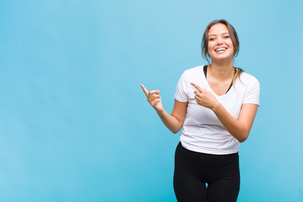 Young hispanic woman smiling happily and pointing to side and upwards with both hands showing object in copy space