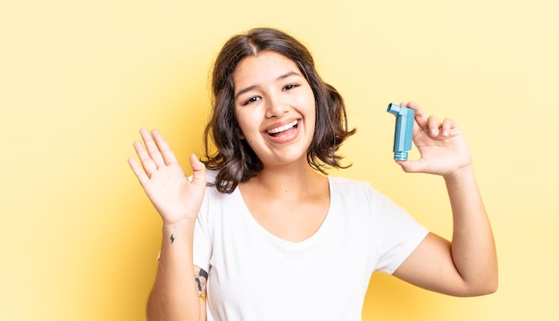 Young hispanic woman smiling happily waving hand welcoming and greeting you asthma concept