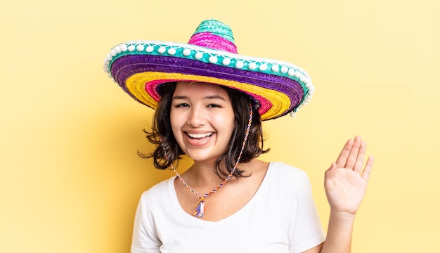 Young hispanic woman smiling happily waving hand welcoming and greeting you mexican hat concept