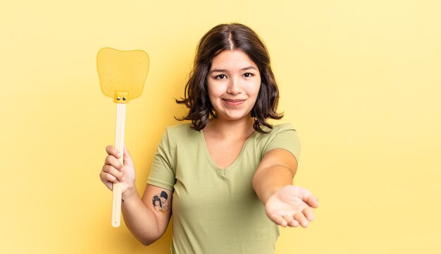 Giovane donna ispanica che sorride felicemente con amichevole e offrendo e mostrando un concetto. concetto di uccidere le mosche