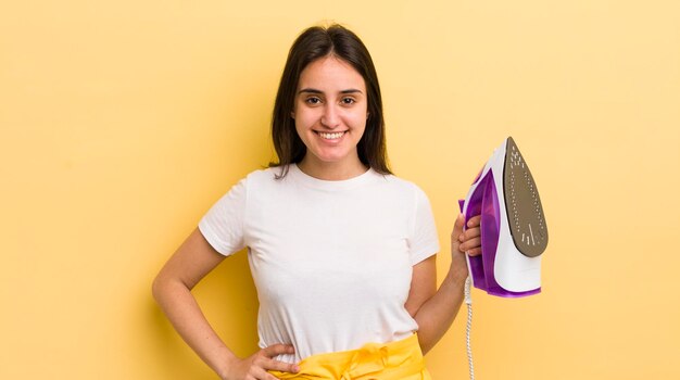 Young hispanic woman smiling happily with a hand on hip and confident clothes iron concept