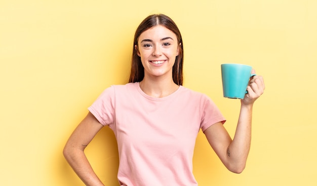 Giovane donna ispanica che sorride felicemente con una mano sull'anca e fiduciosa. concetto di tazza di caffè