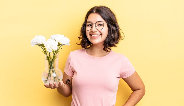young hispanic woman smiling happily with a hand on hip and confident. flowers pot concept