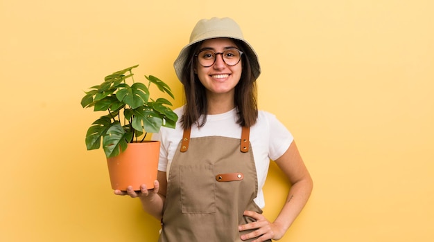 ヒップと自信を持って庭師と植物の概念に手を添えて幸せそうに笑っている若いヒスパニック系女性
