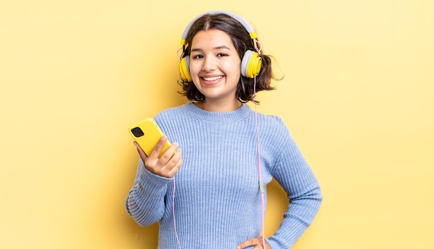 Young hispanic woman smiling happily with a hand on hip and confident. headphones and smartphone concept