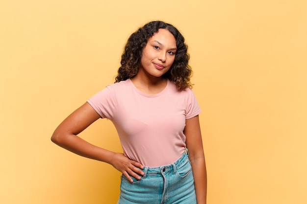 Young hispanic woman smiling happily with a hand on hip and confident, positive, proud and friendly attitude