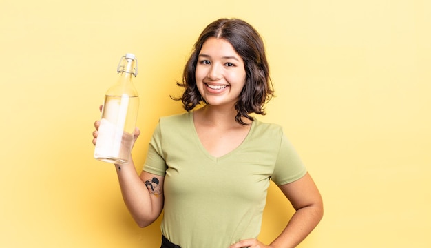 Young hispanic woman smiling happily with a hand on hip and confident. water bottle concept