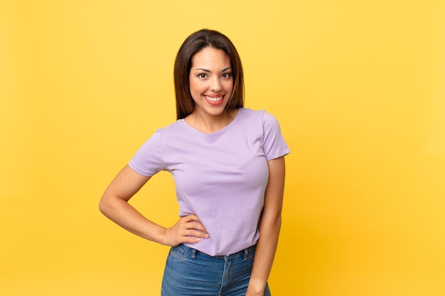 young hispanic woman smiling happily with a hand on hip and confident