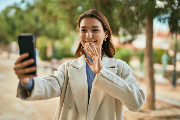 公園でスマートフォンを使ってビデオ通話をしながら幸せに微笑む若いヒスパニック系女性