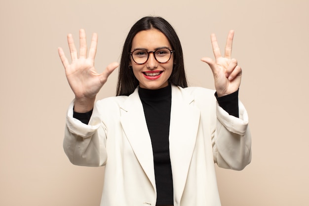 Young hispanic woman smiling and looking friendly, showing number eight or eighth with hand forward, counting down