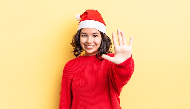 Young hispanic woman smiling and looking friendly, showing number five. christmas concept