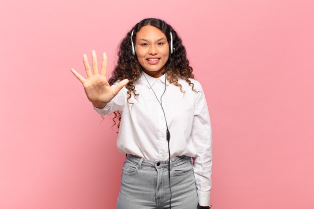 Young hispanic woman smiling and looking friendly, showing number five or fifth with hand forward, counting down. telemarketer