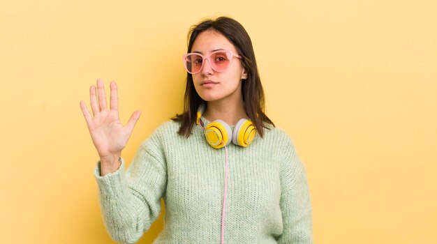 Young hispanic woman smiling and looking friendly showing number five headphones and sunglasses concept