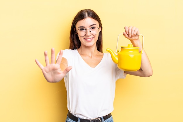 Young hispanic woman smiling and looking friendly, showing number five. teapot concept