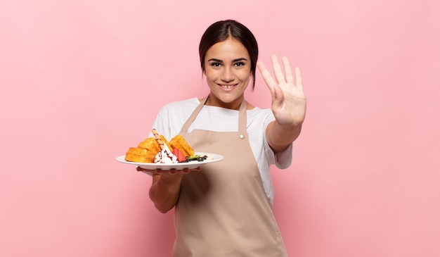 Giovane donna ispanica sorridente e dall'aspetto amichevole, mostrando il numero quattro o quarto con la mano in avanti, il conto alla rovescia