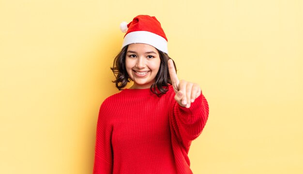 Young hispanic woman smiling and looking friendly, showing number one. christmas concept