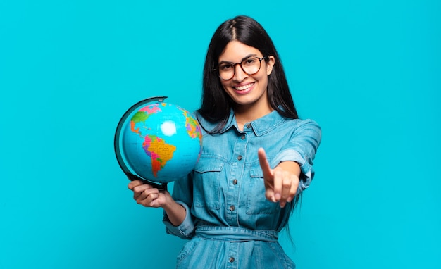 Young hispanic woman smiling and looking friendly, showing number one or first with hand forward, counting down. earth planet concept