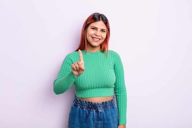 Young hispanic woman smiling and looking friendly, showing number one or first with hand forward, counting down