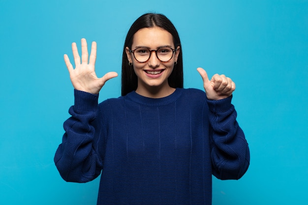 Young hispanic woman smiling and looking friendly, showing number six or sixth with hand forward, counting down