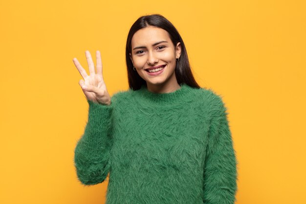 Young hispanic woman smiling and looking friendly, showing number three or third with hand forward, counting down