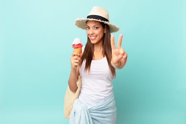 Young hispanic woman smiling and looking friendly, showing number two and holding an ice cream. sumer concept