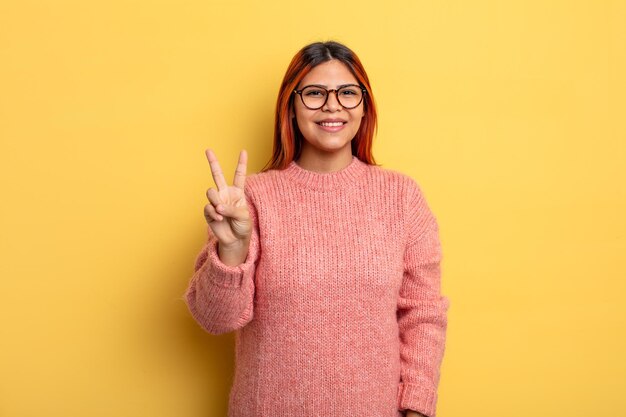 young hispanic woman smiling and looking friendly, showing number two or second with hand forward, counting down