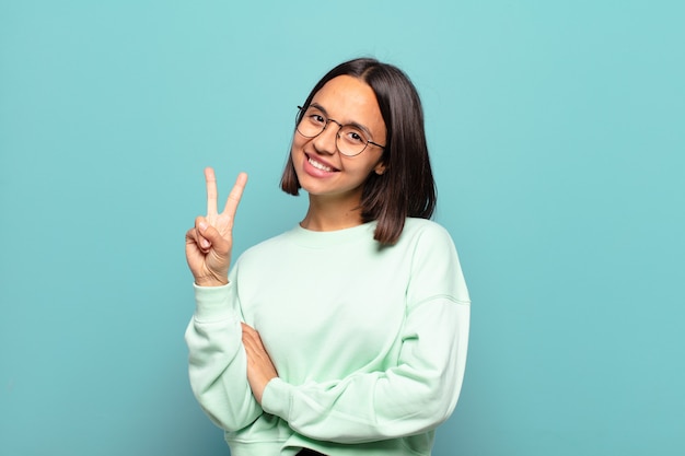 Young hispanic woman smiling and looking friendly, showing number two or second with hand forward