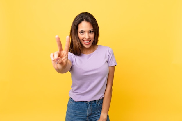 Young hispanic woman smiling and looking friendly, showing number two