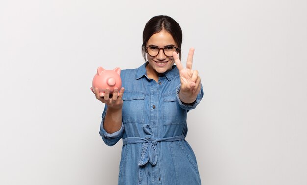 Young hispanic woman smiling and looking happy, carefree and positive, gesturing victory or peace with one hand