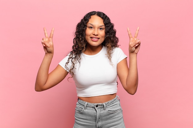 Young hispanic woman smiling and looking happy, friendly and satisfied, gesturing victory or peace with both hands