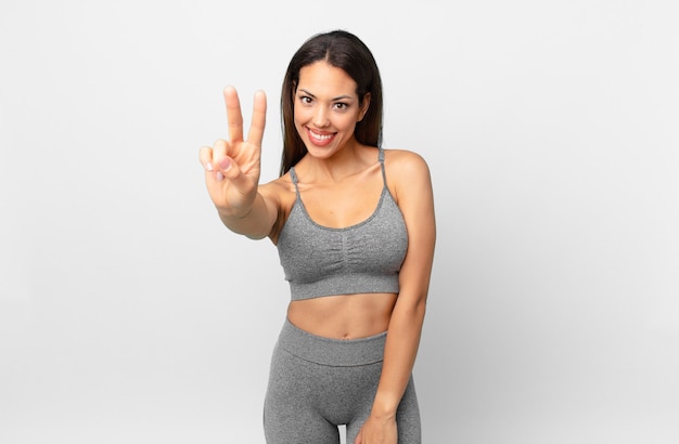 Young hispanic woman smiling and looking happy, gesturing victory or peace. fitness concept