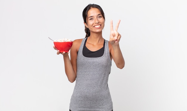 Young hispanic woman smiling and looking happy, gesturing victory or peace. fitness diet and breakfast concept