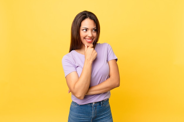 Young hispanic woman smiling with a happy, confident expression with hand on chin